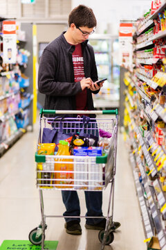 Young man in his 20s doing the family grocery shop checking the shopping list on his phone