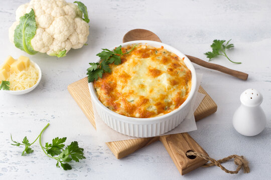 Homemade cauliflower casserole with cheese on a light gray background with ingredients. Delicious vegetarian food