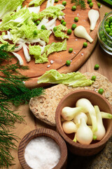Obraz na płótnie Canvas vegetables on a wooden kitchen board, green onions, dill and peas, sliced cabbage on a wood background, concept of fresh and healthy food, still life