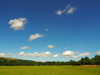 Fototapeta premium Sports ground with green grass and blue sky with clouds on sunny day in Ballincollig Park, Cork, Ireland