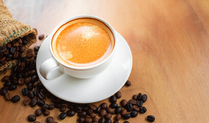 Top view of coffee cup has golden foam and mixed or blend coffee beans in a brown sack on wooden backgrou