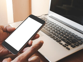 Smartphone white screen mockup on a man hand on laptop computer black keyboard white phone screen mock-up on a desk office with copy space. The concept for using an advertising banner text.