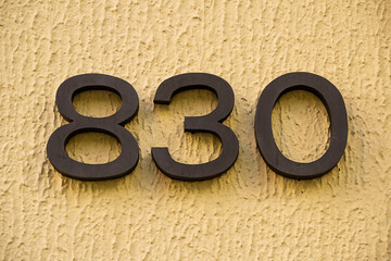 Número oitocentos e trinta em metal pregado na parede de um prédio. 830.