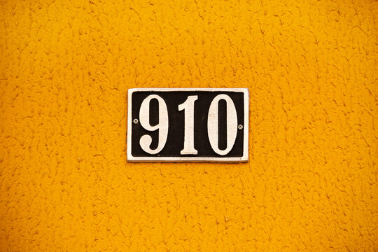 N&uacute;mero novecentos e dez em metal pregado na parede de um pr&eacute;dio com parede amarela. 910.