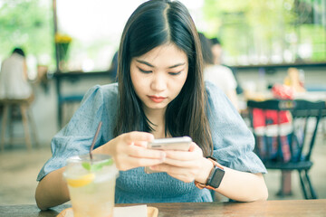 Beautiful asian women typing text on smartphone sitting in cafe