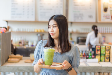 Asian smiling women with ice matcha green tea in art cafe