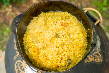 an elderly man cooks pilaf in a pot on a tandoor stove.