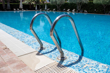 Swimming pool with stairs in the hotel. View of the tropical garden and swimming pool with sun...