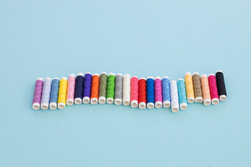 Panoramic detailed view of multi colored spools of thread on a blue background.