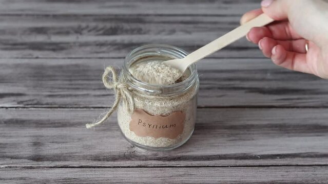 Psyllium is the husk of a plantain. Jar with a spoon and a sticker with the word Psyllium on a wooden background.