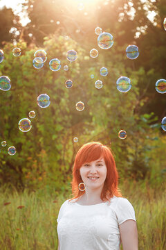 Happy young redhead woman with soap bubbles in the sun. Symbol of freedom and enjoyment.