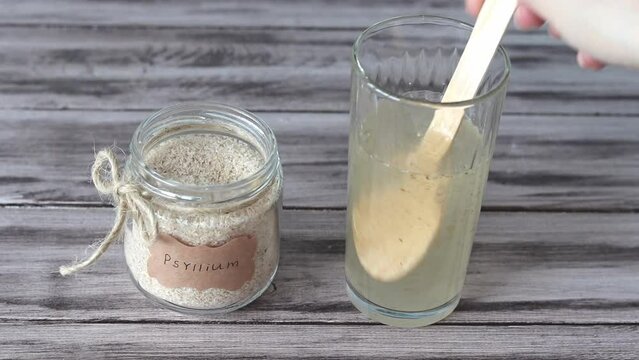 Psyllium is the psyllium husk. A hand stirs psyllium in a glass of warm water.