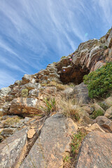 Cliff at the side of mountain or island with cave to rest in after rock climbing, surrounded by plants, trees and nature in summer or spring. Closeup view from the bottom of a canyon with a blue sky