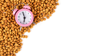 A frame made of dry cat (dog) food and a pink alarm clock on a white isolated background. Space for text. Balanced nutrition. Morning time to feed pets. Template for the design.