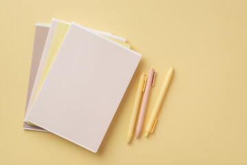 School accessories concept. Top view photo of stationery copybooks and pens on isolated pastel yellow background