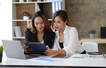 Attractive Asian businesswoman and secretary colleague discussing working on a business project at an office desk.