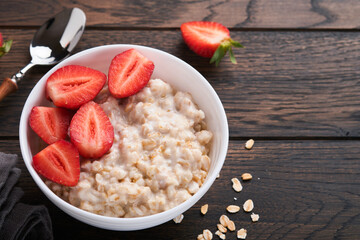 Oatmeal. Bowl of oatmeal porridge with strawberry, almond and milk on old wooden dark table background. Top view in flat lay style. Natural ingredients. Hot and healthy breakfast and diet food.