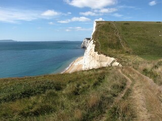 the jurassic coast in england with the white cliffs along the blue sea and a steep hill with a hiking path - the south west coast path