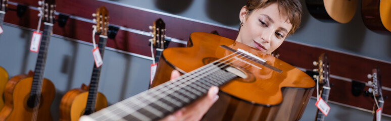 Musician looking at blurred acoustic guitar in music store, banner.