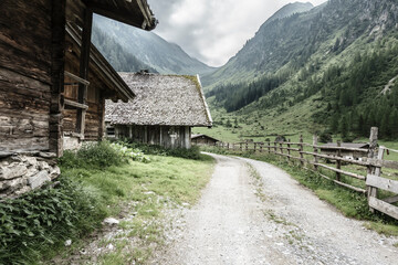 Schotterstraße entlang eines Holzzaunes in den Alpen