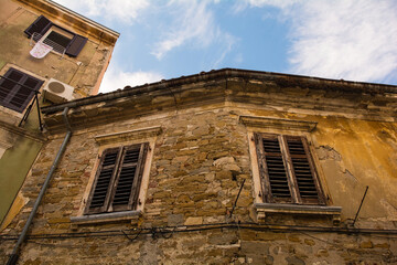 Fototapeta na wymiar Shuttered windows in a derelict stone residential building in the medieval centre of Izola, Slovenia 