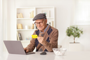 Cheerful elderly man paying with a credit card on a laptop computer