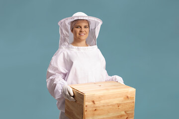 Female bee keeper holding a wooden box isolated on blue