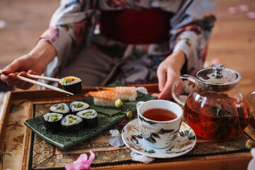 Young woman in japanese kimono holds rolls and sushi with Japanese chopsticks
