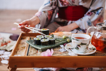 Young woman in japanese kimono holds rolls and sushi with Japanese chopsticks