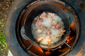 an elderly man cooks pilaf in a pot on a tandoor stove.