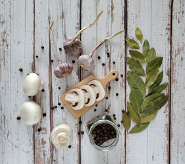 Mushrooms, bay leaf, allspice, garlic, wooden cutting board, glass jar with spices on a light wood background. Top view.