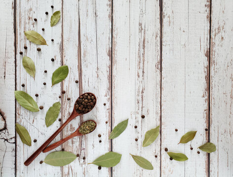 Wooden spoons with allspice and seasoning of Italian herbs, bay leaf on a light wooden background.