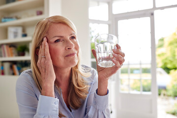 Menopausal Mature Woman At Home Suffering With Headache Pain Drinking Glass Of Water
