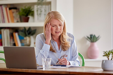Fototapeta na wymiar Menopausal Mature Woman Working On Laptop At Home Suffering With Headache Pain