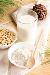 Glass of cedar milk, nuts, cedar flour in white bowl with wooden spoon in napkin on wooden table.