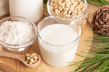 Cedar milk glass, flour and nuts on wooden board close up. Soft focus. Horizontal orientation.