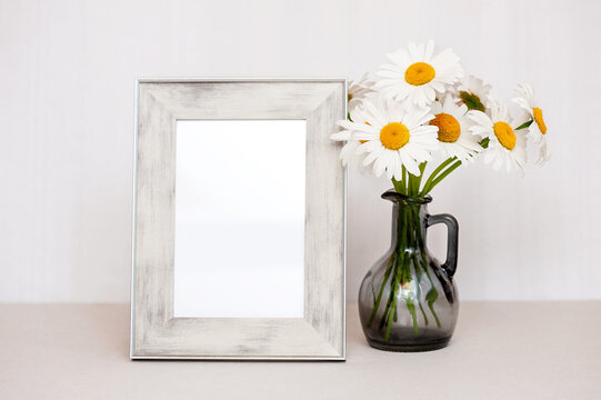A bouquet of white daisies in a vase and a photo frame on the table.