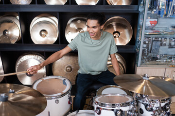 Smiling african american customer playing drums in music shop.