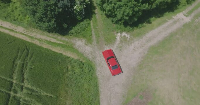 Cinema Drone over head shoot of a 67' construction year Buick Riviera, making a U-Turn on on country road, right next to a forrest.