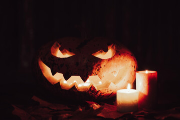Dark photo of jack-o-lantern lit by candles with scary smile looking to the camera. Halloween concept