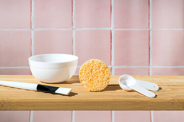 Bathroom wooden shelf with beauty accessories like brush, spoon, sponge and mask making plate on a pink tile wall tile. Morning skin care ritual. Eco friendly sustainable beauty product. Copy space.
