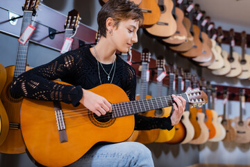Side view of customer playing acoustic guitar in instrumental music shop.