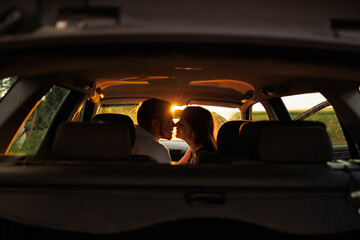 Romantic couple in sunlight from sunset kissing while sitting in car during trip