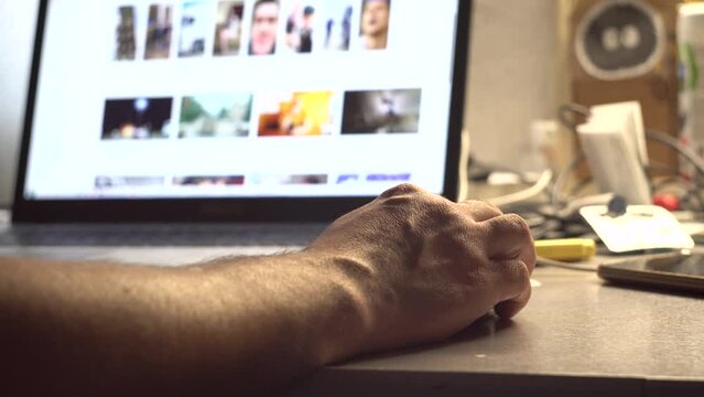 A man watches content on a computer screen. Laptop on the table. Receiving the information. Photo and video content.. Surfing on the Internet. Tester. User. IT-specialist. Close-up.