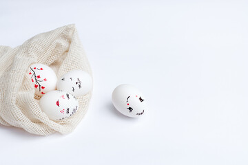 Easter beautifully painted eggs in ecological mesh bag on white table. Funny faces, flowers, gentle...