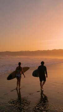 AERIAL SILHOUETTE: Two surfers carrying surfboards and checking waves after surf session. Surf friends walking on the beach in golden light. Gorgeous summer scenery at Playa Venao in Panama.