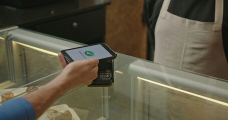 Closeup hand paying with phone in contactless payment. NFC technology in a restaurant. Closeup hands of mobile payment at a coffee shop