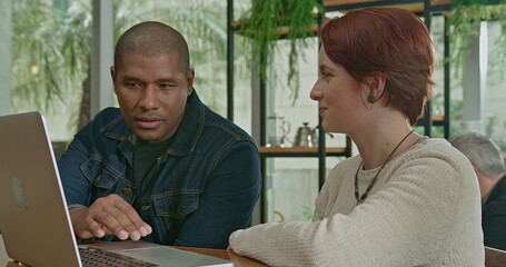 Two diverse young people in front of laptop at coffee shop. Woman pointing at computer screen with a black colleague