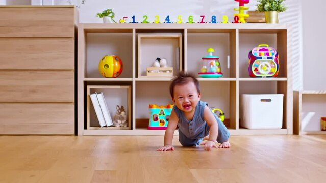 Healthy asian baby toddler crawling on floor to learn to crawl indoors. Adorable baby keeping her belly and legs down on the floor to belly crawl fun and happiness at home. Nursery room