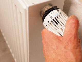 Hand turns the thermostat of a radiator, save energy, reduce energy costs, heating concept
